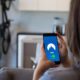 Person sits on a sofa holding a smartphone that shows a VPN app with a blue screen and mountain logo, indicating a connection.