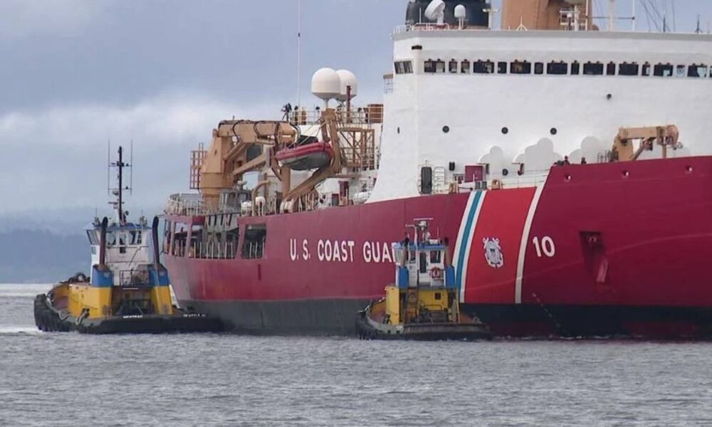 Coast Guard vessel being guided by two tugboats in a harbor.