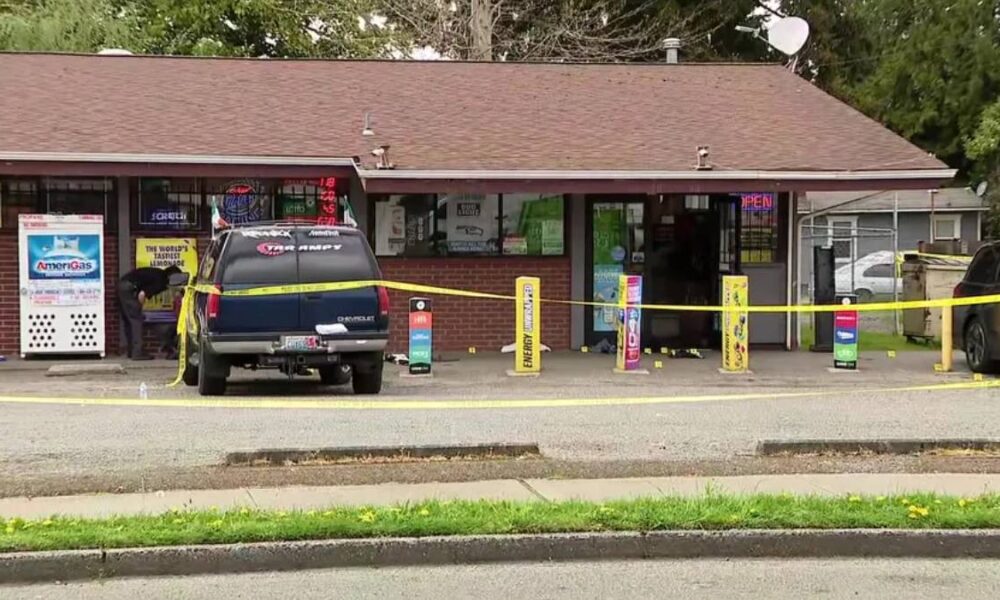 A blue SUV parked in front of a small shop, yellow caution tape stretched across the scene, storefront windows and vending machines visible behind it.