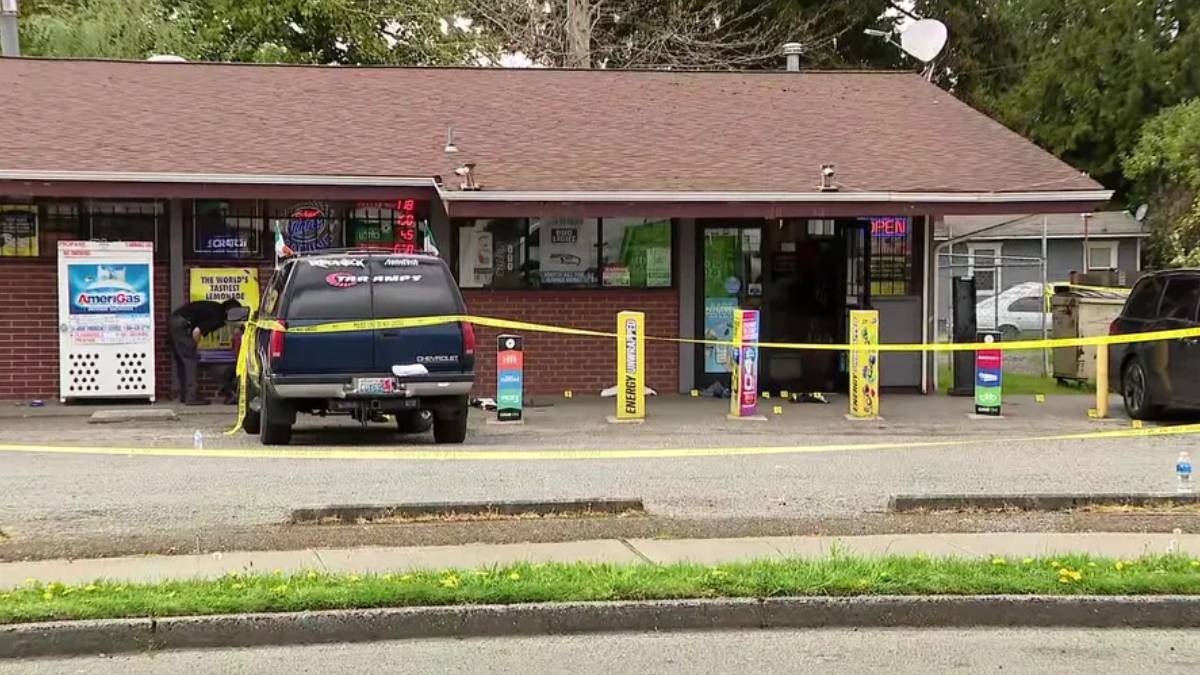 A blue SUV parked in front of a small shop, yellow caution tape stretched across the scene, storefront windows and vending machines visible behind it.
