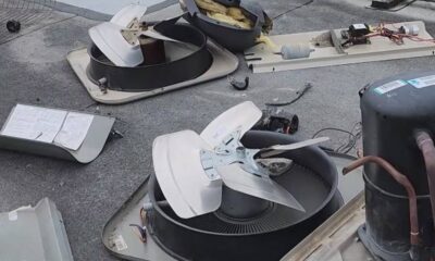 Disassembled rooftop HVAC unit parts scattered on a flat roof, including a large ceiling fan-like blower and wiring pieces