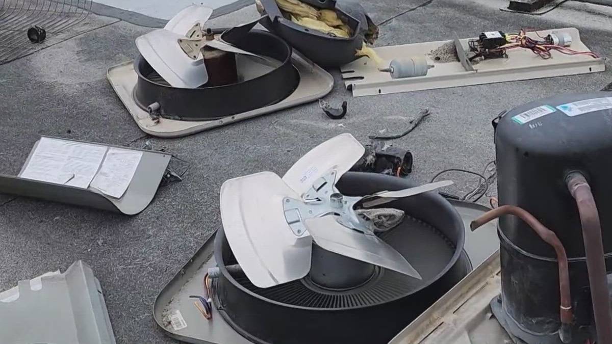 Disassembled rooftop HVAC unit parts scattered on a flat roof, including a large ceiling fan-like blower and wiring pieces