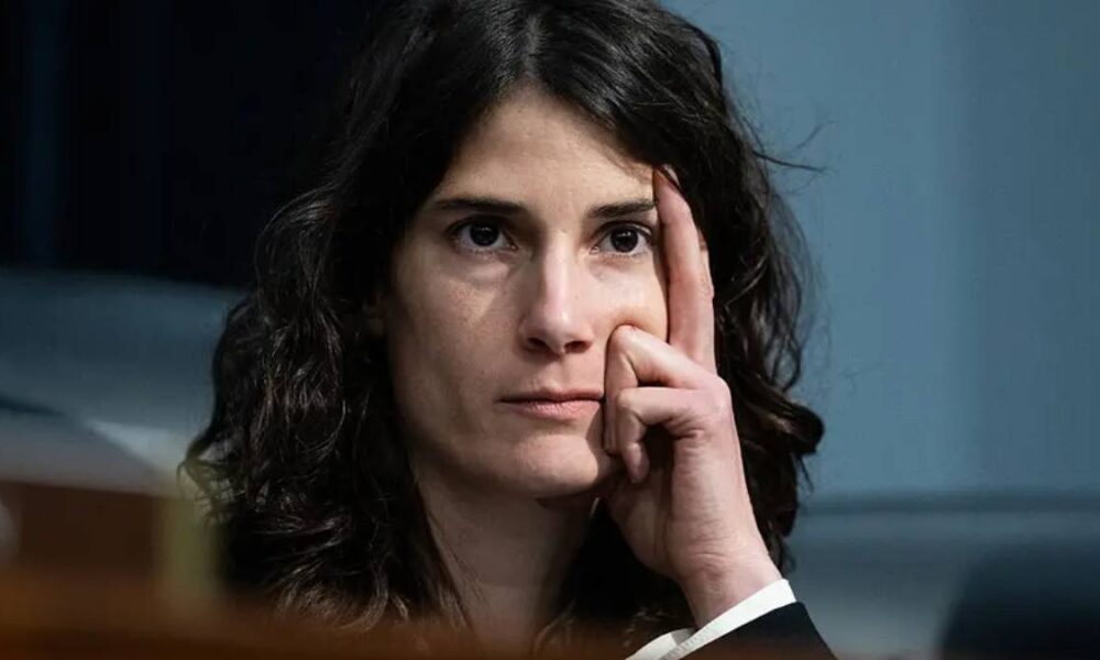 Woman with dark hair touching her temple, looking thoughtful.