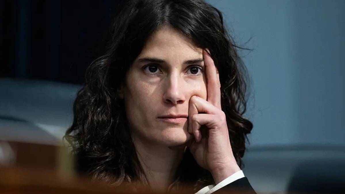 Woman with dark hair touching her temple, looking thoughtful.