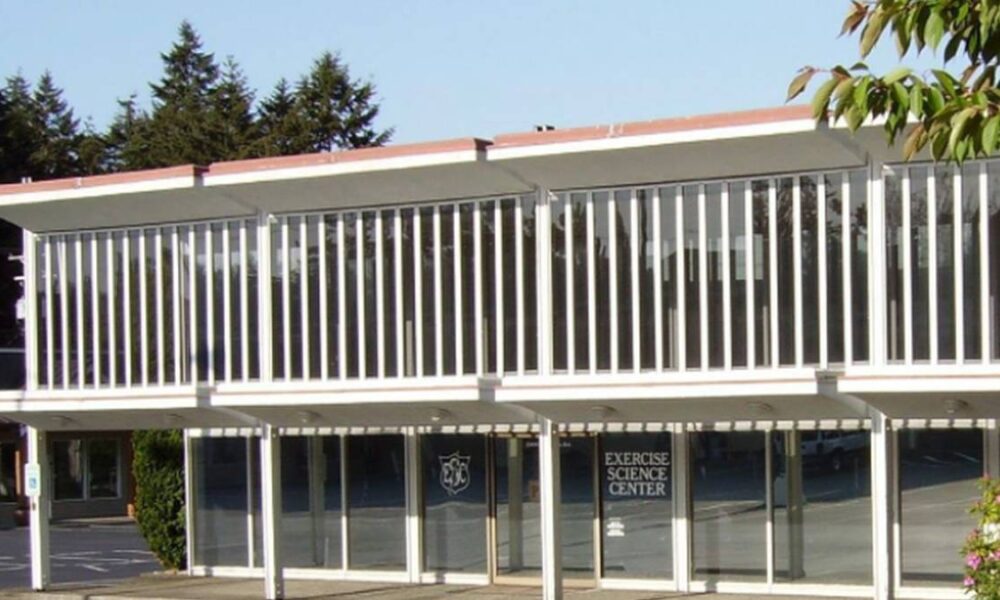 Two-story modern building with glass storefront on the ground floor and a second-floor balcony enclosed by white vertical slats; sign reads Exercise Science Center on the door/window.
