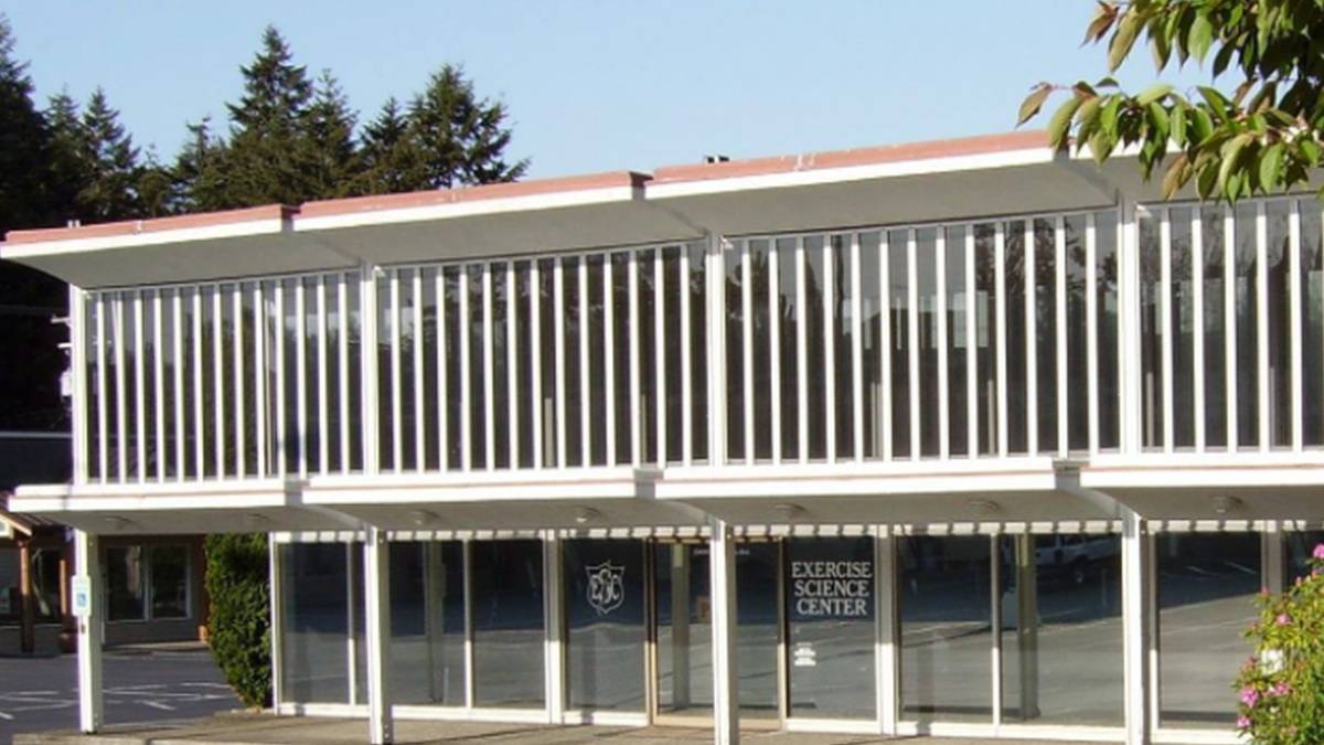 Two-story modern building with glass storefront on the ground floor and a second-floor balcony enclosed by white vertical slats; sign reads Exercise Science Center on the door/window.