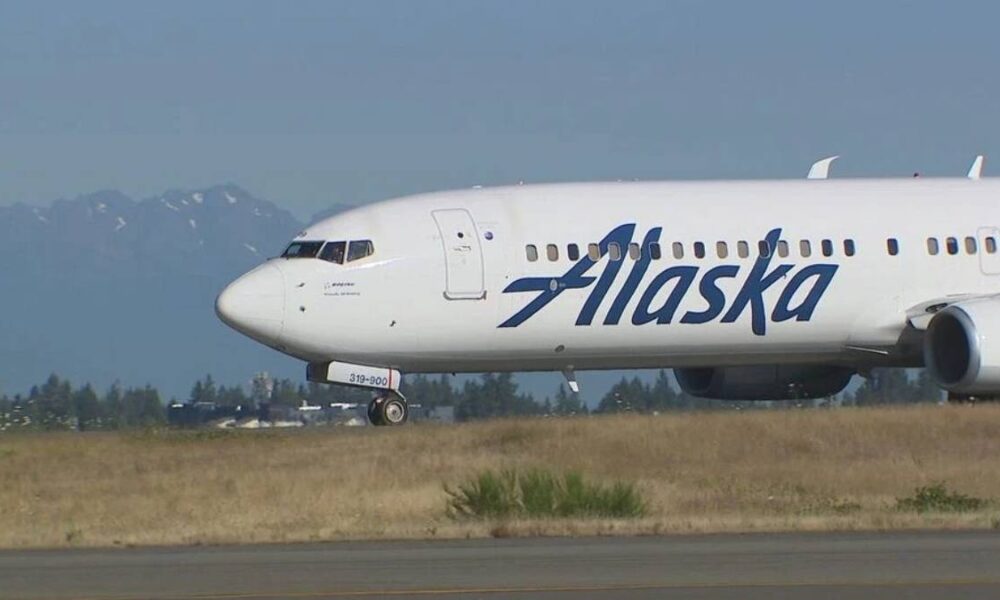 Side view of an Alaska Airlines jet on the runway with mountains in the background.