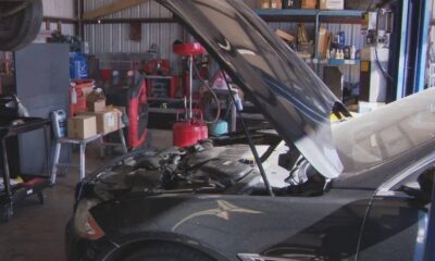 Car in an auto repair shop with its hood raised, engine visible and tools around in the background