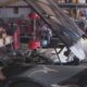 Car in an auto repair shop with its hood raised, engine visible and tools around in the background