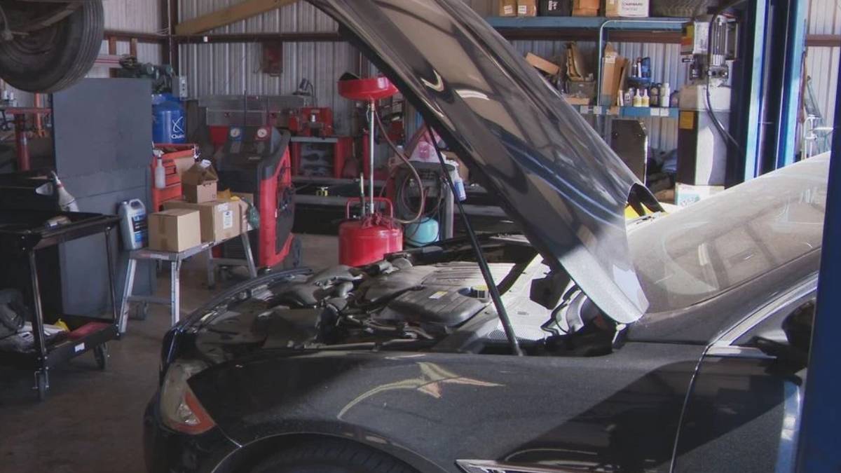 Car in an auto repair shop with its hood raised, engine visible and tools around in the background