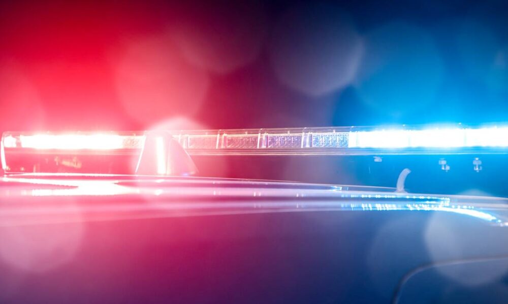 Red and blue emergency lights flashing on a police car at night, creating bokeh reflections in the foreground.