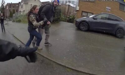 Girl grabs the arm of a man as they walk on a wet residential street; a parked car is nearby, viewed from a dashcam perspective.