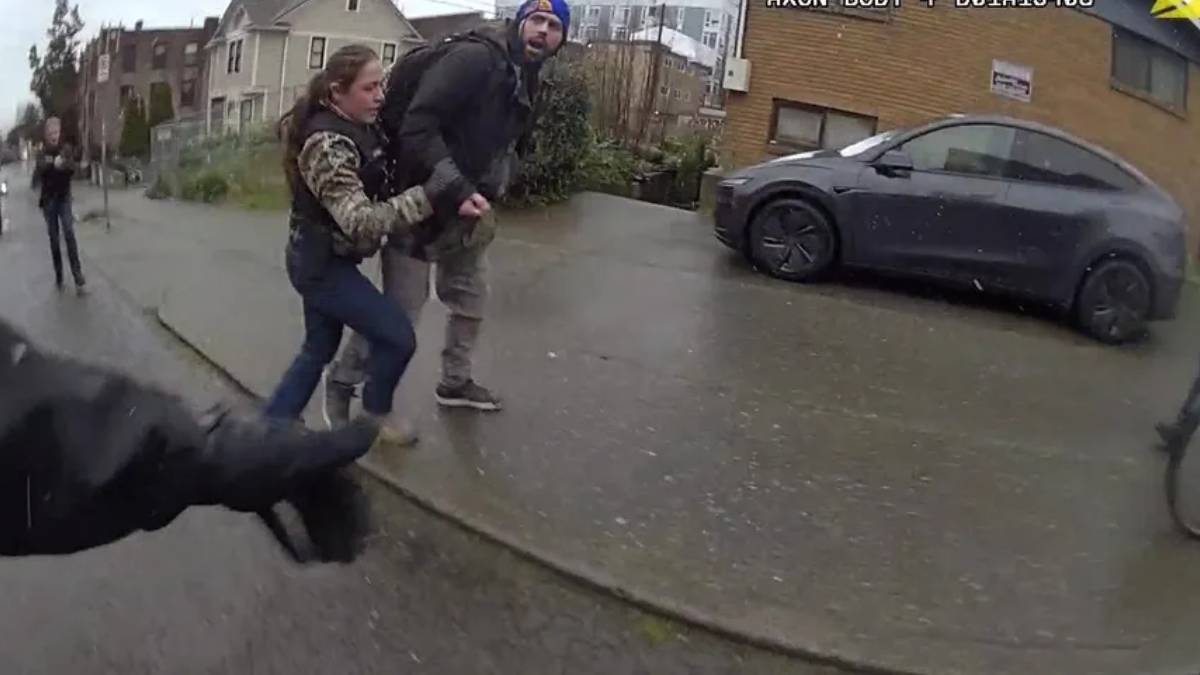 Girl grabs the arm of a man as they walk on a wet residential street; a parked car is nearby, viewed from a dashcam perspective.