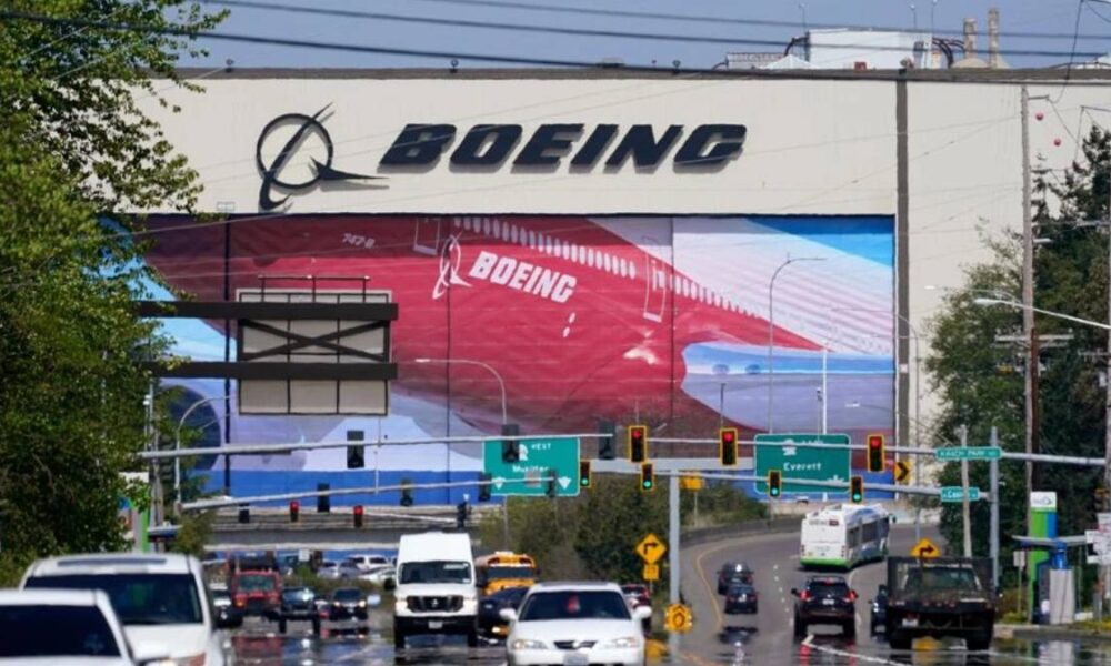 Boeing billboard towering over a busy multi-lane road with cars and green directional signs below.