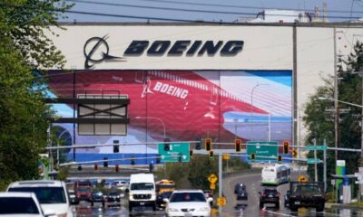Boeing billboard towering over a busy multi-lane road with cars and green directional signs below.