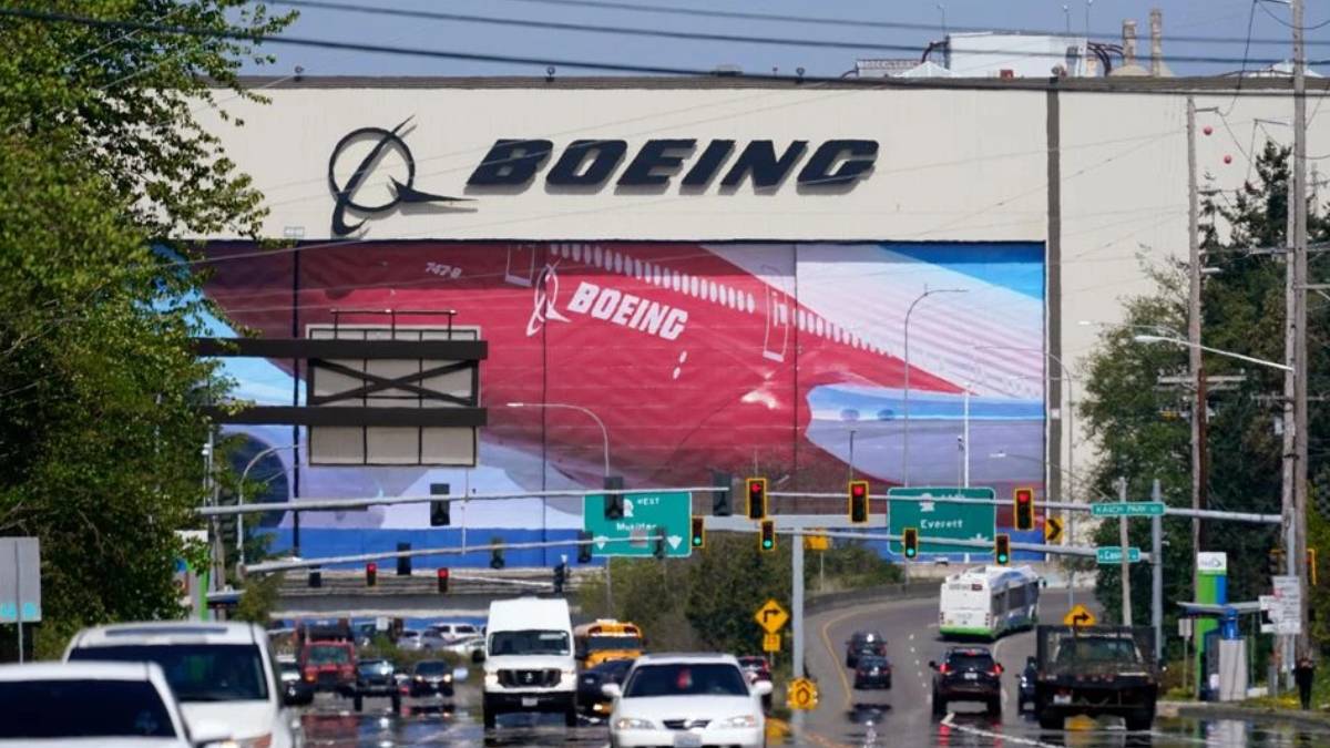 Boeing billboard towering over a busy multi-lane road with cars and green directional signs below.