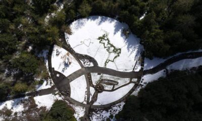 Aerial view of a circular snow-covered park with dark winding paths and surrounding trees.