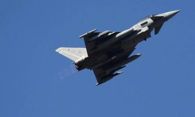 Fighter jet photographed from below as it climbs against a clear blue sky, viewed from beneath.