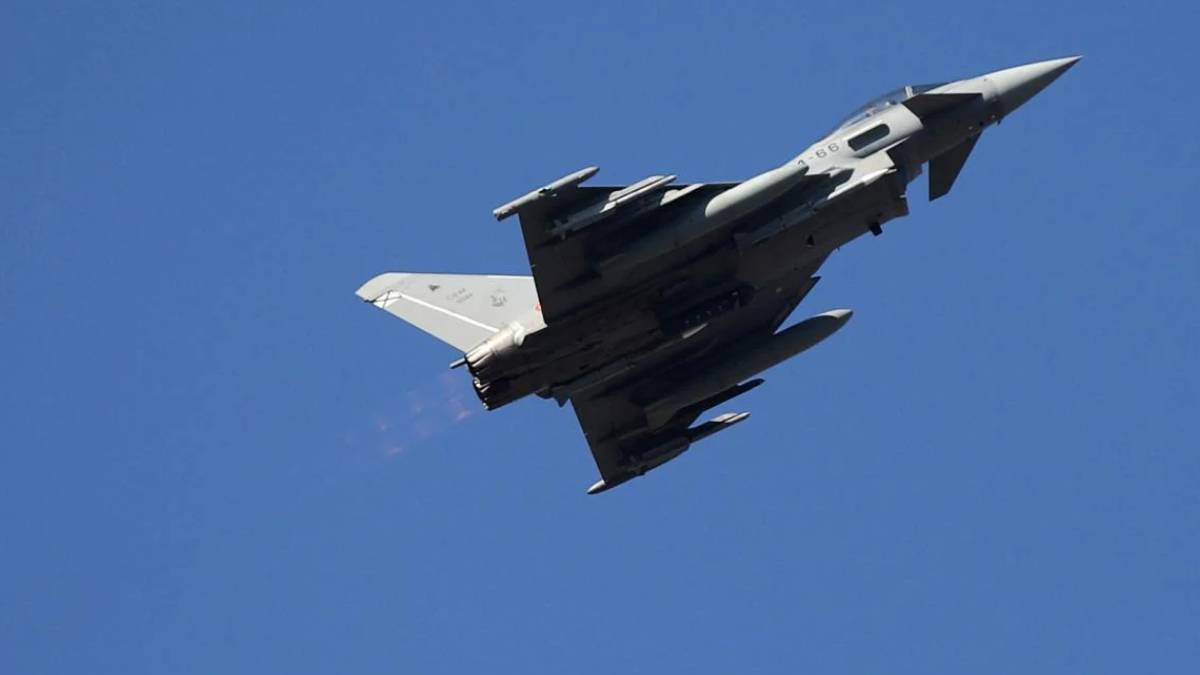Fighter jet photographed from below as it climbs against a clear blue sky, viewed from beneath.