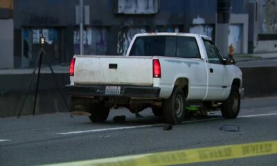 White pickup truck on a city street behind yellow caution tape, with a tripod-mounted camera set up nearby behind it.