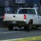 White pickup truck on a city street behind yellow caution tape, with a tripod-mounted camera set up nearby behind it.