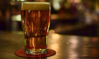 A pint of amber beer with a foamy head on a wooden bar, resting on a red coaster.