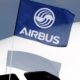 Blue Airbus flag with white logo fluttering near the tail of a white commercial airplane, casting a shadow on the fuselage.