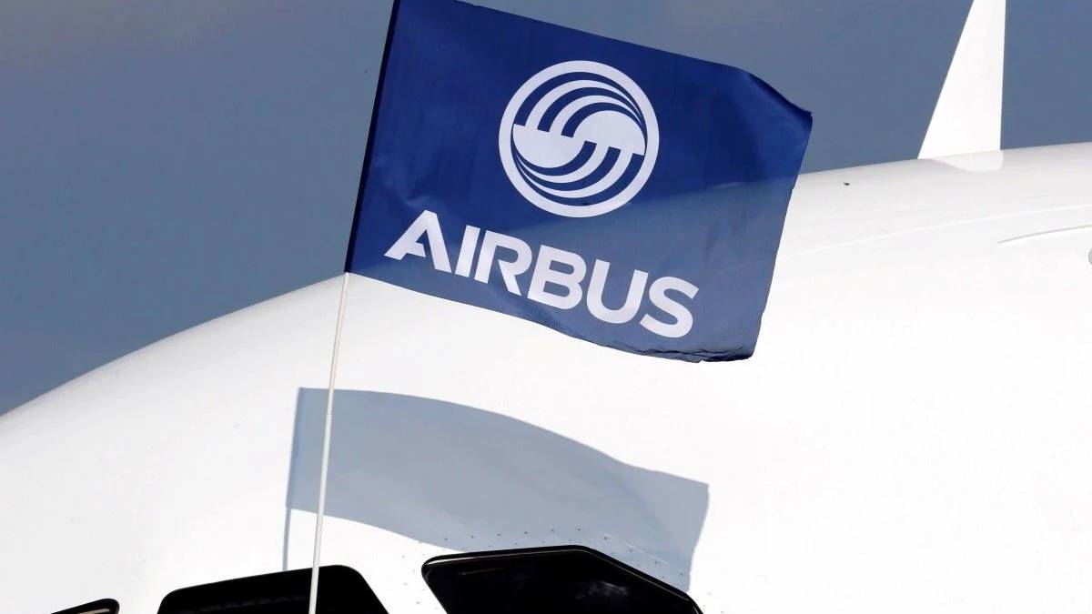 Blue Airbus flag with white logo fluttering near the tail of a white commercial airplane, casting a shadow on the fuselage.