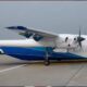 Small white and blue AirLink aircraft parked on a taxiway, showing a high-wing design and front propeller.