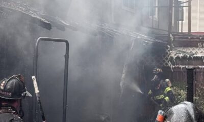 Firefighters in turnout gear spraying water in a smoky backyard fire scene.