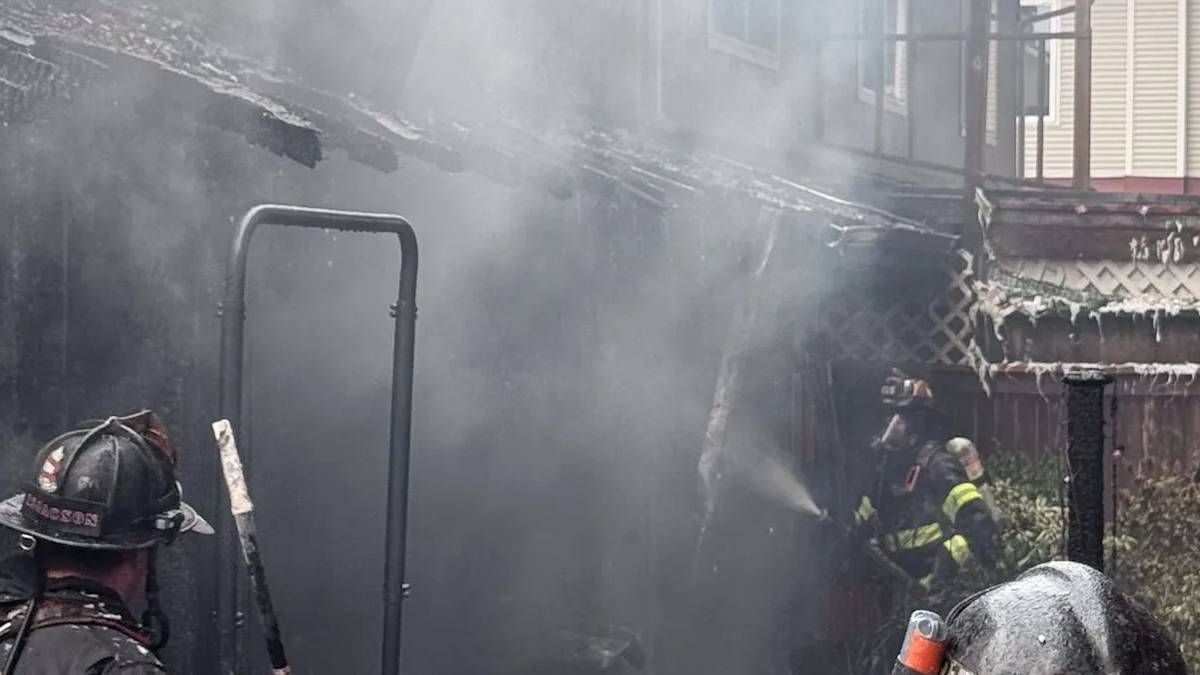 Firefighters in turnout gear spraying water in a smoky backyard fire scene.