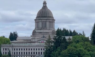 State capitol building with a large dome, set against a cloudy sky and trees in the foreground.