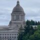 State capitol building with a large dome, set against a cloudy sky and trees in the foreground.