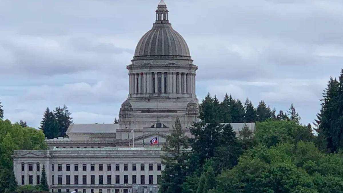 State capitol building with a large dome, set against a cloudy sky and trees in the foreground.