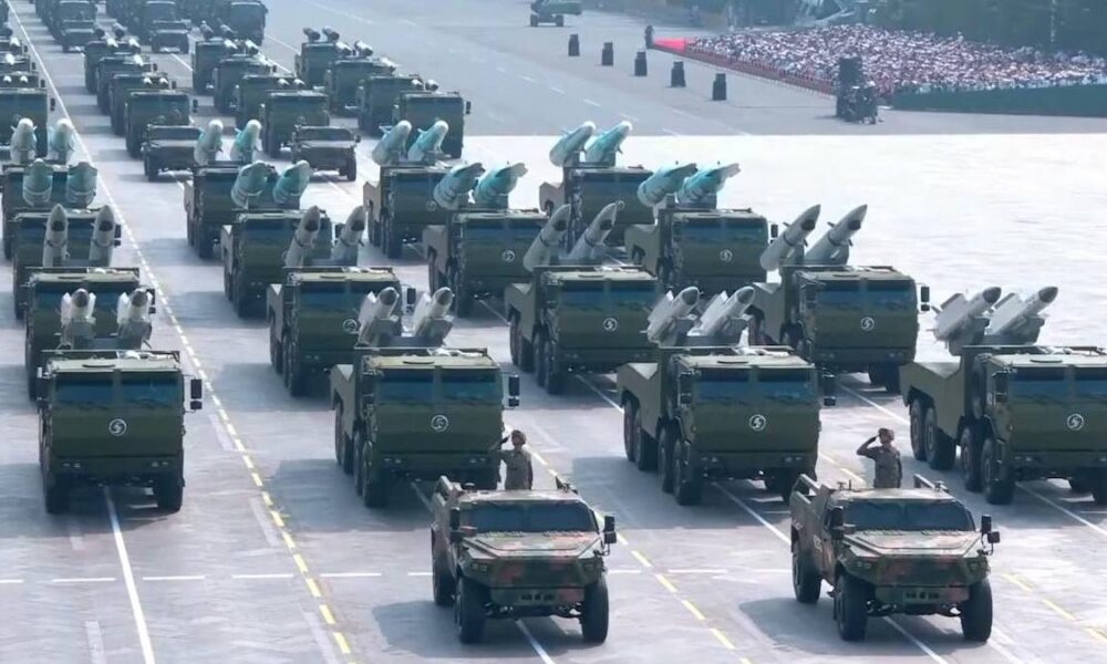Ranked rows of green missile-carrying trucks in a military parade on a wide runway, with soldiers nearby.