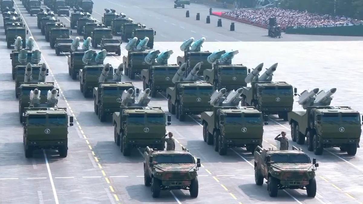 Ranked rows of green missile-carrying trucks in a military parade on a wide runway, with soldiers nearby.