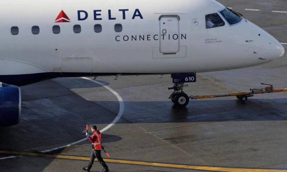 Delta Connection regional airliner on the tarmac, ground crew member in a bright vest signaling with a baton nearby.