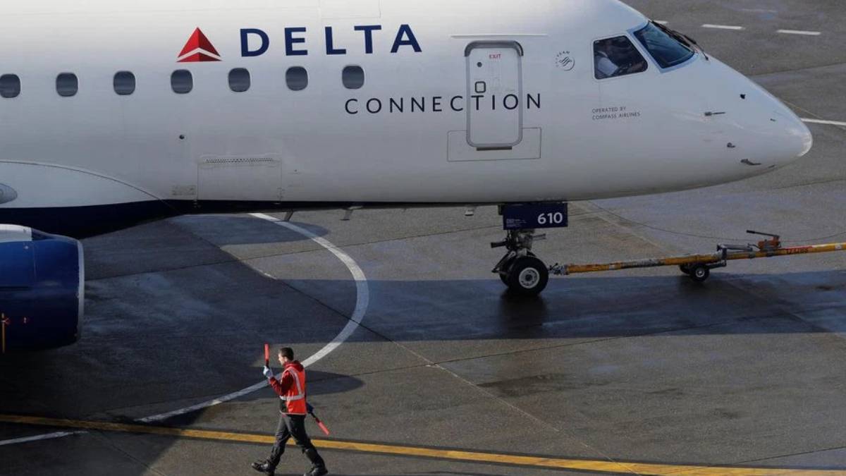 Delta Connection regional airliner on the tarmac, ground crew member in a bright vest signaling with a baton nearby.