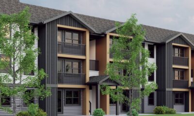Modern townhouse building with three stories, black/gray siding, orange-brown trim, and balconies surrounded by trees.