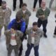 Group of veterans in camouflage jackets standing in a circle indoors, each holding a red rose.