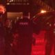 Nighttime street scene with police officers and a patrol SUV with flashing red lights.