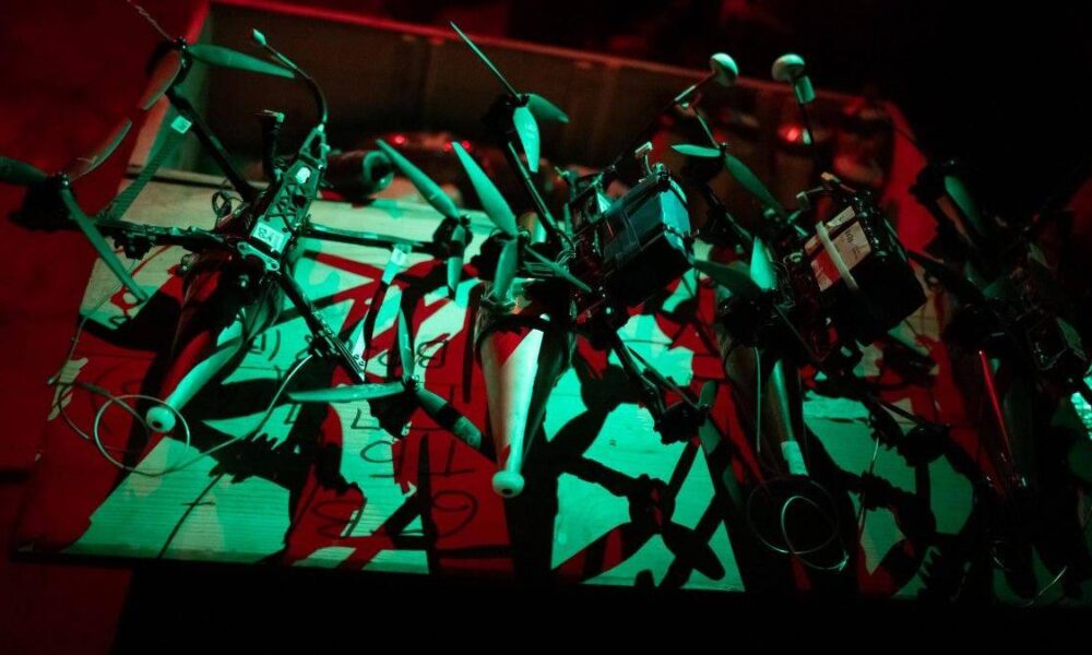 Abstract wall sculpture made of metal frames, pipes, and handles suspended on a bar, bathed in red and green lighting.
