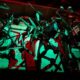 Abstract wall sculpture made of metal frames, pipes, and handles suspended on a bar, bathed in red and green lighting.