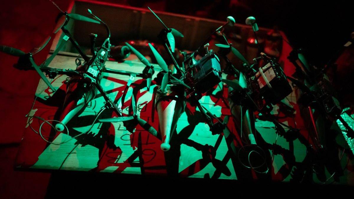 Abstract wall sculpture made of metal frames, pipes, and handles suspended on a bar, bathed in red and green lighting.