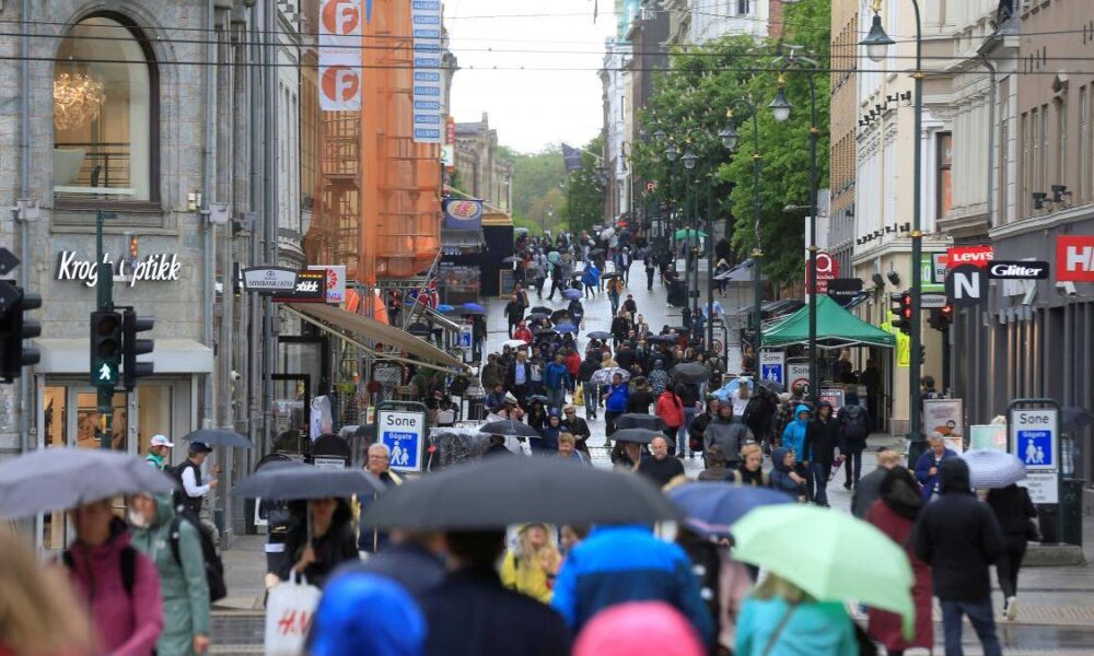 Busy city shopping street on a rainy day crowded with pedestrians and umbrellas.