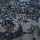 Aerial view of a town submerged in floodwater, with streets and yards filled and houses surrounded by water.