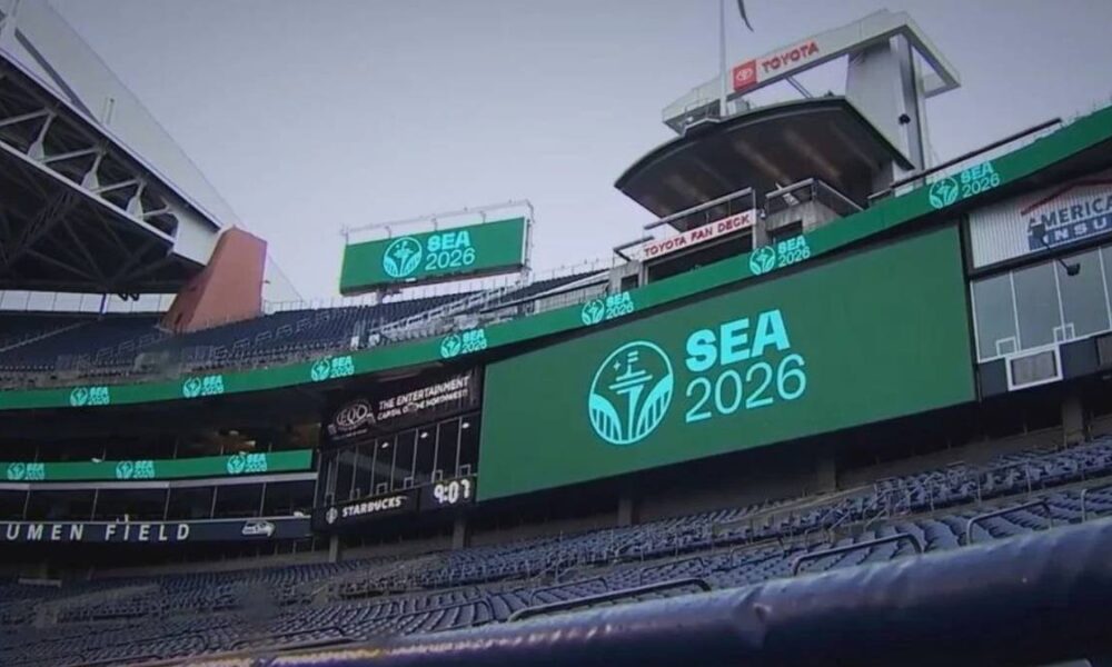 Large SEA 2026 logo on a stadium video board at Lumen Field, with empty blue seats surrounding it.