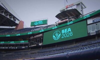 Large SEA 2026 logo on a stadium video board at Lumen Field, with empty blue seats surrounding it.