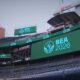 Large SEA 2026 logo on a stadium video board at Lumen Field, with empty blue seats surrounding it.