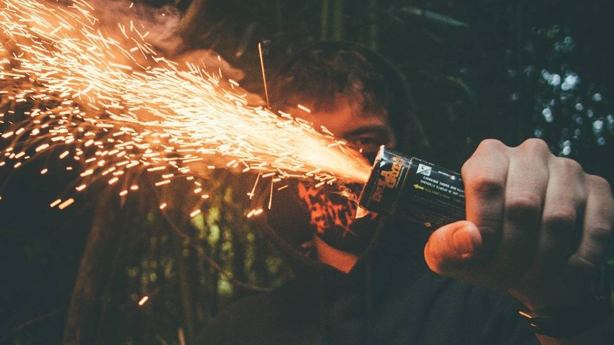 Person holding a handheld spark-emitting device, sparks shooting outward in a dark outdoor setting.